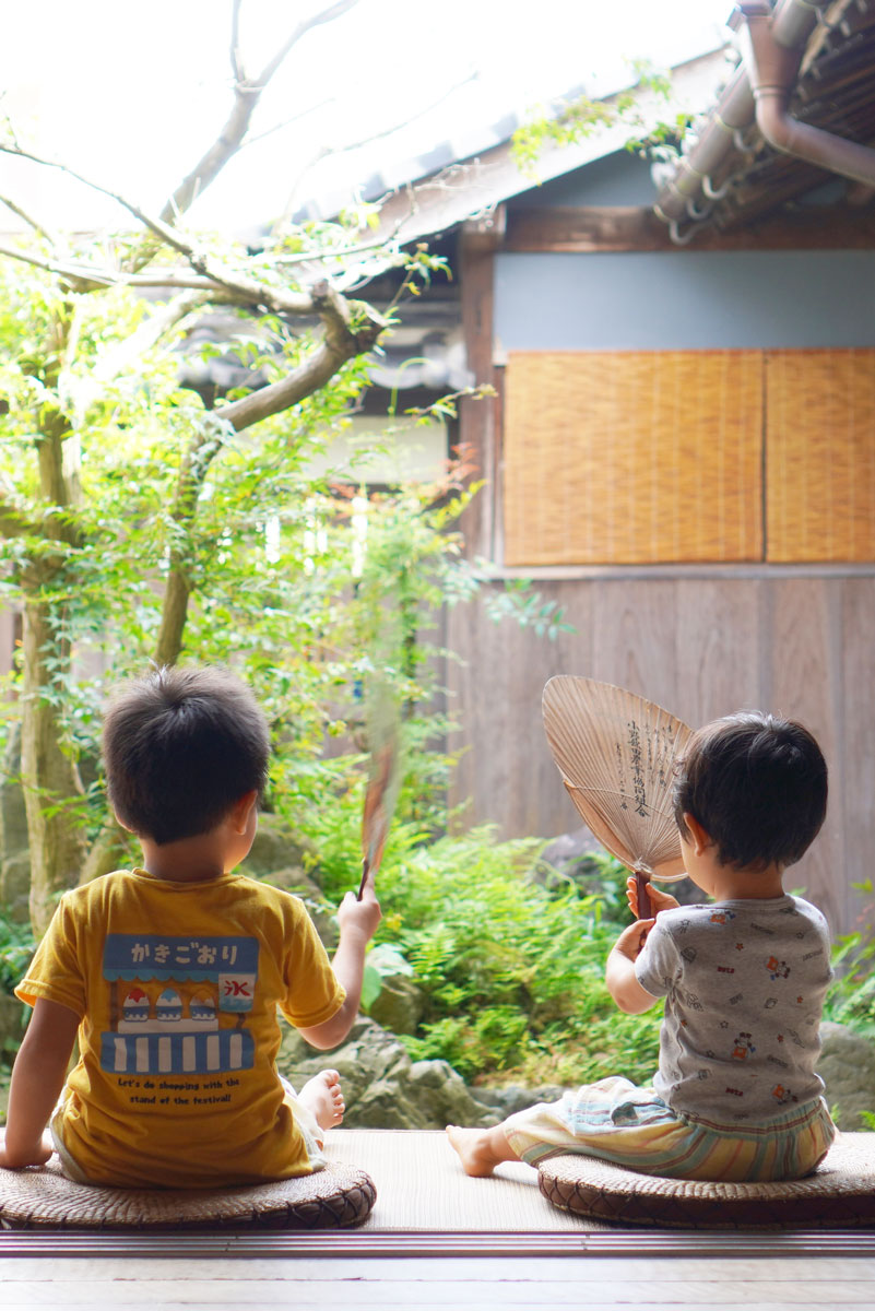 緑側で2人の子どもがうちわをパタパタしている様子